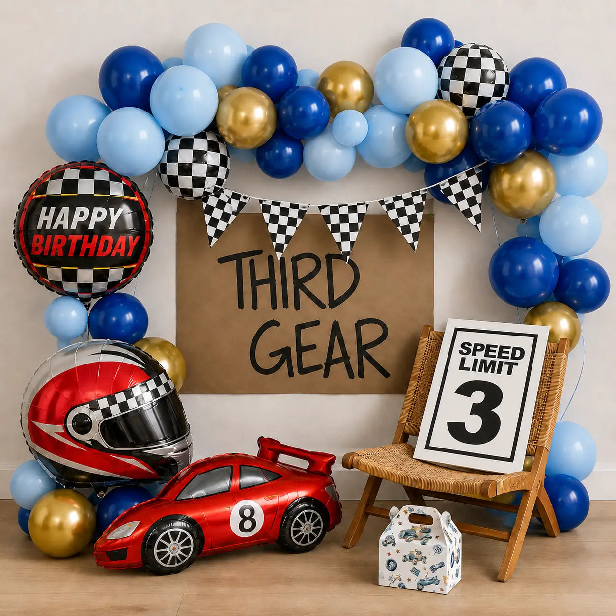 Third Gear race car birthday party backdrop with blue and gold balloons, checkered flags, helmet and race car balloons