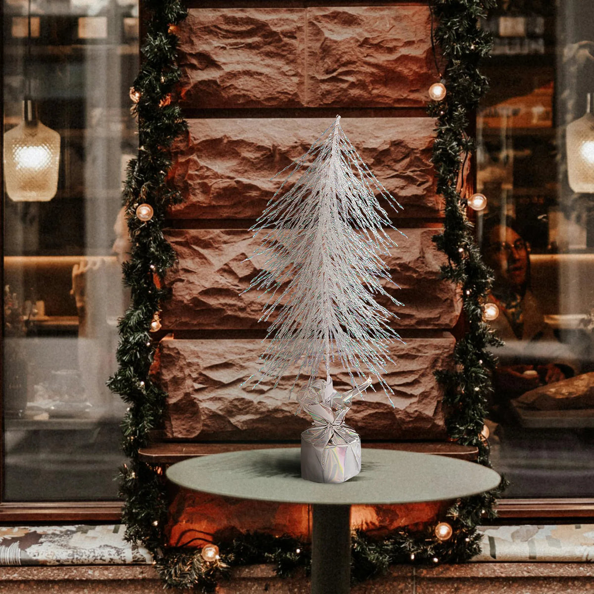 An iridescent tabletop tree stands on a small table before a fireplace.