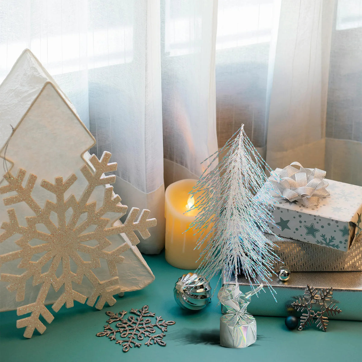 An iridescent tree sits among a gift box and other winter decorations.