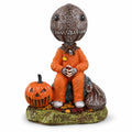 Trick-or-treat child figurine seated beside a carved pumpkin and candy sack.