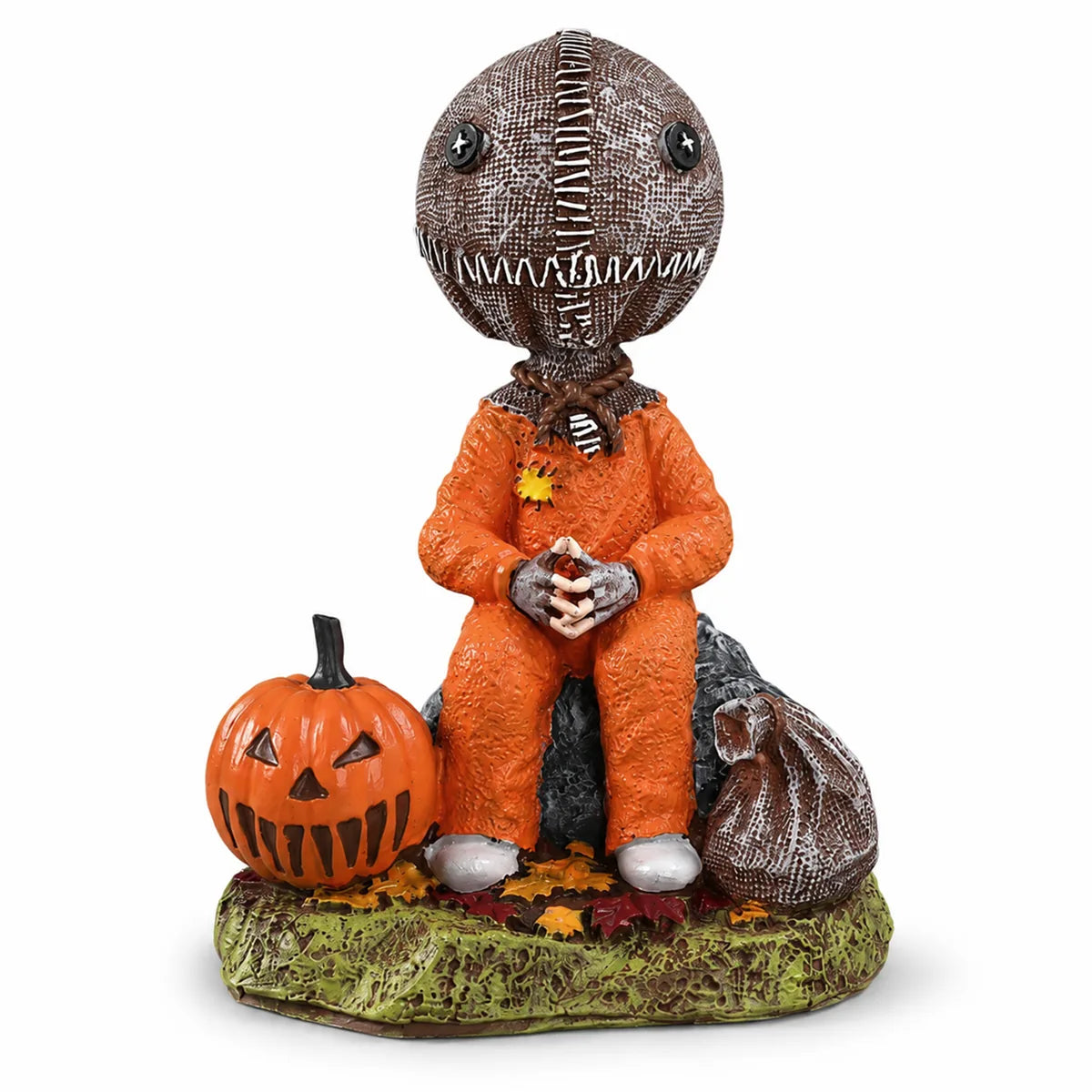 Trick-or-treat child figurine seated beside a carved pumpkin and candy sack.