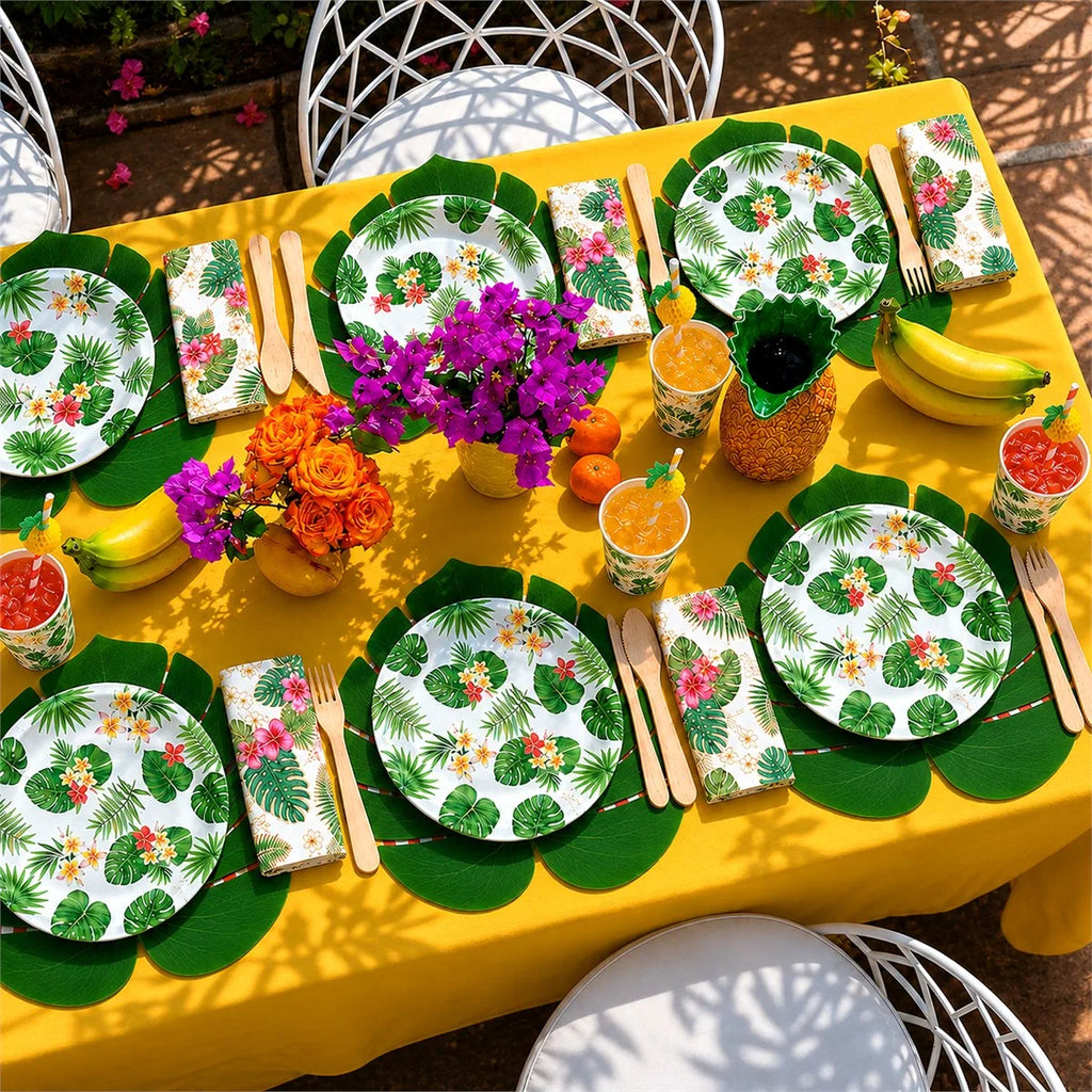 Tropical party table setup with floral plates, paper cups, napkins, and wooden cutlery