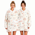 Two adults sharing a cream cat print oversized hoodie blanket with twin hoods and a shared front pocket.