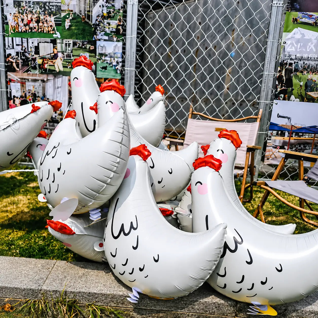Group of white chicken-shaped foil balloons displayed outdoors near a fence and chairs